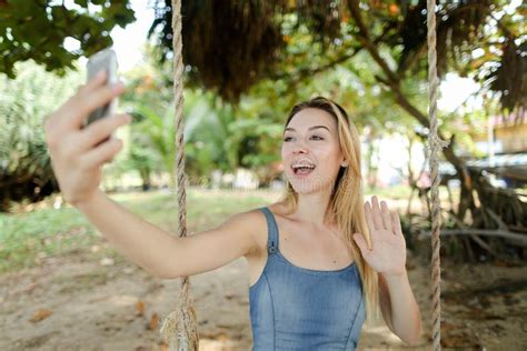 Young Woman Riding Swing And Making Selfie By Smartphone Sand And Trees In Background Stock