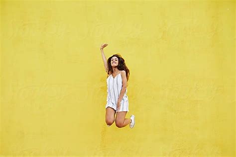 Smiling Girl In Dress Jumping Over Yellow Wall By Stocksy Contributor Guille Faingold