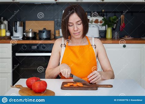 Young Beautiful Woman In Apron Sitting At Table Cooking At Home