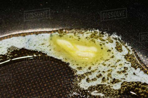 Close Up Of Piece Of Butter Slowly Melting And Bubbling In Black Teflon Frying Pan Stock