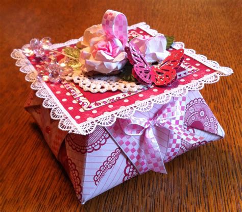 An Origami Box On A Wooden Table With Lace And Flowers In The Center
