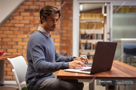 Side View Close Up Of A Young Caucasian Man Sitting At A Desk Using A