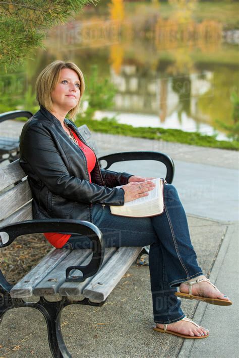 Mature Christian Woman Studying Her Bible In A City Park Setting Beside