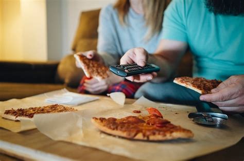pareja comiendo pizza en el sofá de su sala de estar por la noche mientras ve una película en la