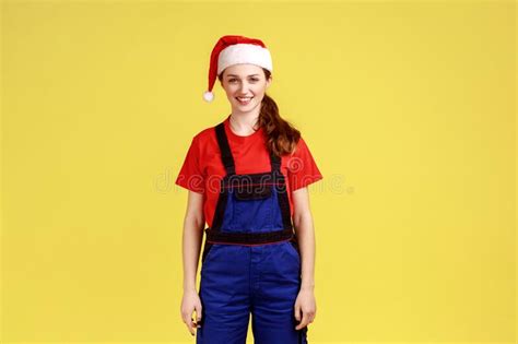 Happy Handy Woman In Blue Overalls And Santa Hat Looking At Camera Profession Of Service