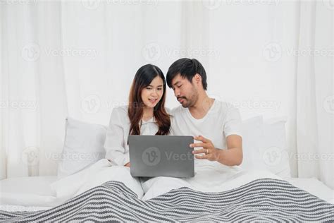 Young Happy Asian Couple Using Laptop In Bed Watching Movie Romantic