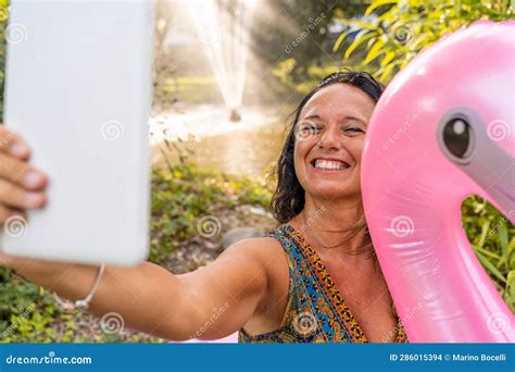 Beautiful Smiling Middle Aged Woman Taking A Selfie Sitting On A Pink Flamingo Inflatable Toy