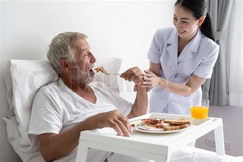 senior man with smiling nurse takes care breakfast and discussion and cheer on bed at nursing