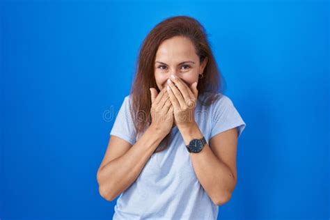 Brunette Woman Standing Over Blue Background Laughing And Embarrassed Giggle Covering Mouth With
