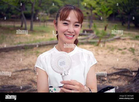 A Mature Japanese Woman Outdoors In A Park On A Hot Day Holding A Small Electric Fan Stock Photo