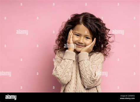 Tender Dreamy Shy Small Girl With Kinky Dark Hair Touching Cheeks With Palms Having Happy