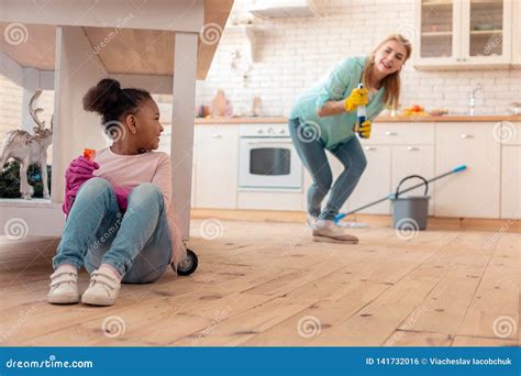 cute curly daughter hiding under table while cleaning flat with mom