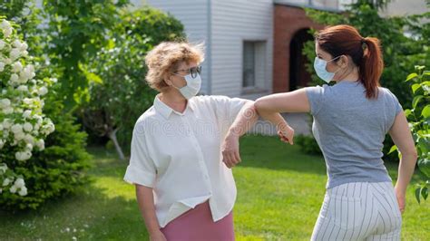 Two Masked Women Greet Their Elbows In The Park An Elderly Woman And