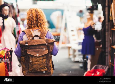 blonde curly hair woman backpacker traveler viewed from rear at used market enjoying the