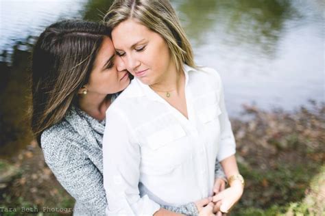 Two Women Standing Next To Each Other In Front Of A Body Of Water And Grass