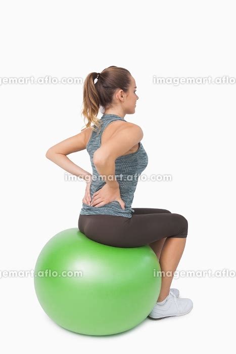Blonde Ponytailed Woman Touching Her Back Sitting On Fitness Ballの写真素材