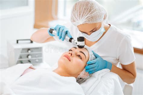 Nice Skilled Female Dermatologist Holding A Dermatoscope Stock Photo