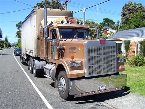 A Large Semi Truck Driving Down The Road In Front Of A House With Power
