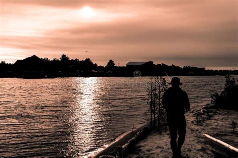 Silhouette Of Guy In Hat Fishing In River On Sunset Editorial