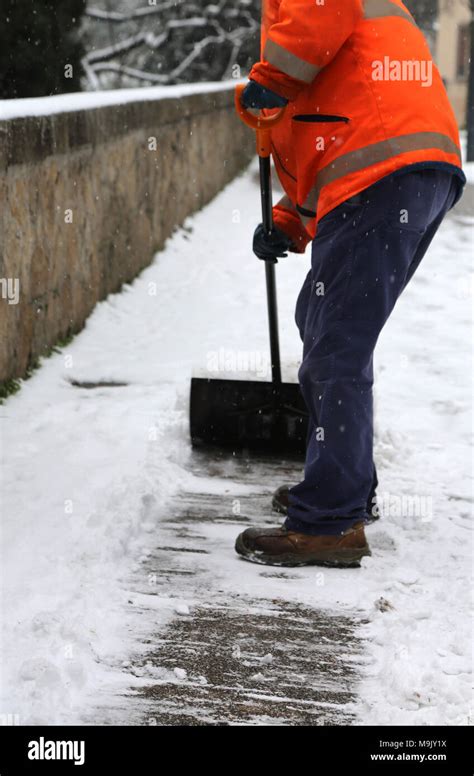 Worker While Shoveling Snow From Frozen Sidewalk After Snowfall In