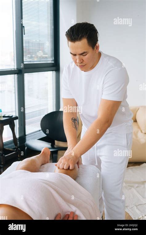Medium Shot Of Professional Male Masseur With Strong Tattooed Hands Massaging Lower Leg Of