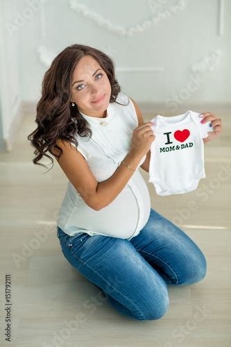 Pregnant Young Brunette Woman In Jeans And White Tshirt Keeping In