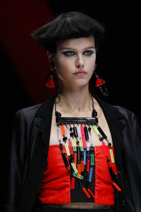 A Woman With Black Hair And Bright Jewelry On Her Neck Is Standing In