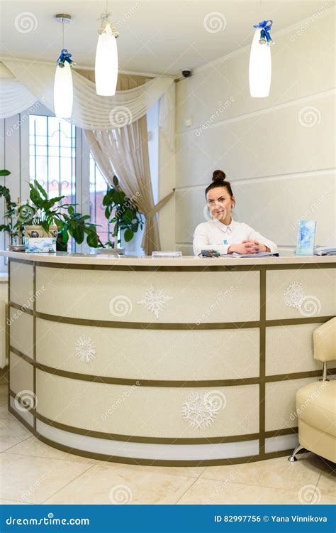 Woman Receptionist In Medical Coat Stands At Reception Desk Stock Photo