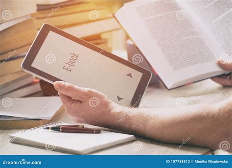 Man Holding A Modern Ebook Reader And Book In Library Stock Photo