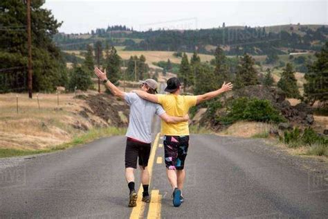 Two Men Walking Along Road Together Arms Raised Appreciating View