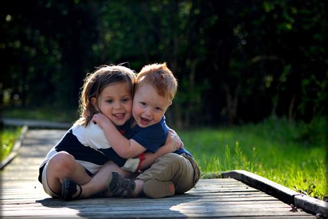 Brother And Sister Hugs Toddler Sibling Poses Outdoor On Low Bridge