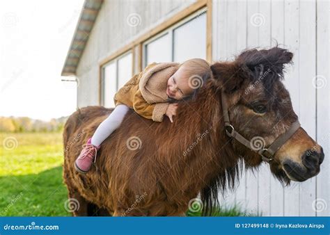 A Cute Baby Girl Is Sitting On A Pony In Village Stock Photo Image