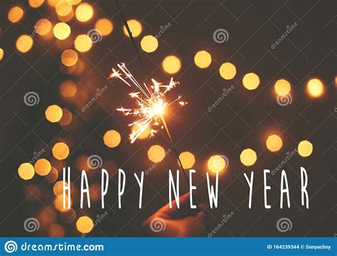 Happy New Year Text Sign On Glowing Sparkler In Hand On Background Of