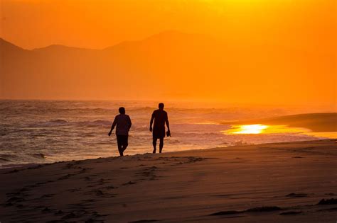 Silhouett Of Two Friends Walking Along Beach During Sunset Siluetas