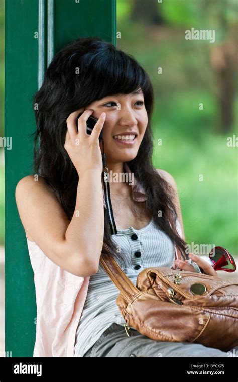 Attractive Young Chinese Woman Speaking On Cellphone In The Grounds Of