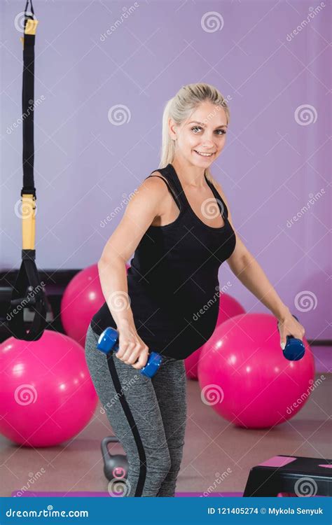 pregnant woman stand in the gym holding her weights on 9 month with lovely eyesight and doing
