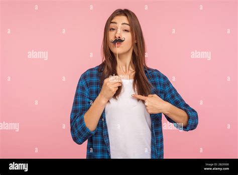 Portrait Of Playful Girl In Checkered Shirt Holding Fake Curly Mustache On Stick And Pointing