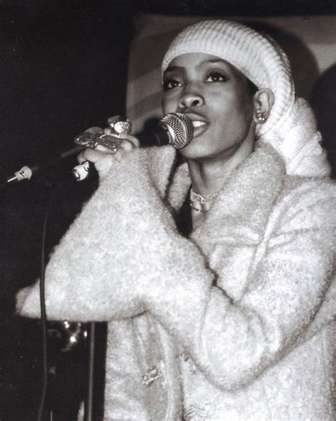 A Black And White Photo Of A Woman Singing Into A Microphone With A Hat On