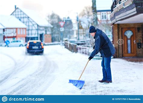 Man With Snow Shovel Cleans Sidewalks In Winter During Snowfall Winter