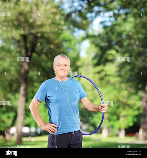 Smiling Mature Athlete With Headphones Holding A Hula Hoop In A Park