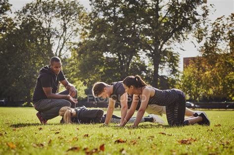 Personal Trainer Instructing Man And Women Doing Push Ups In Park