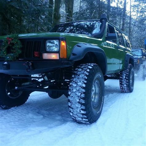 A Green Jeep Parked In The Snow With Christmas Decorations On Its Bumpers