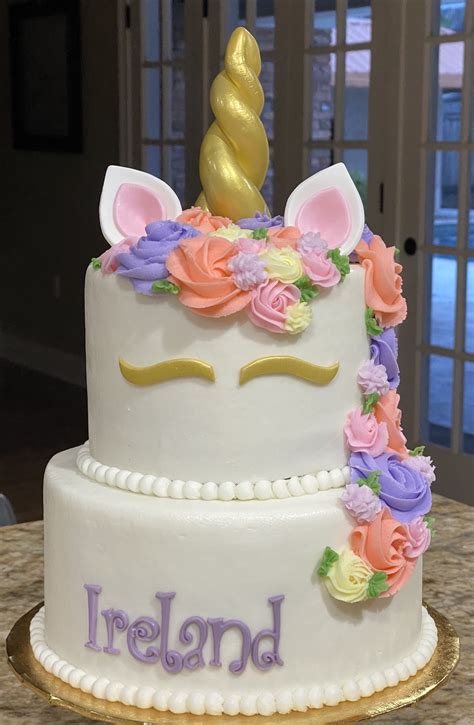 A White Cake Decorated With Flowers And A Unicorn Face