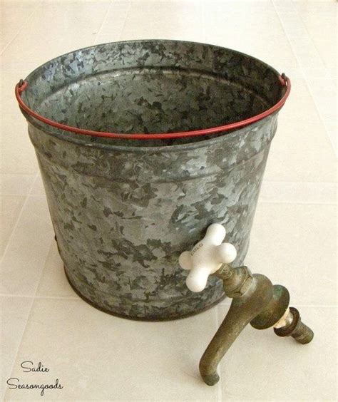 A Metal Bucket With Two White Flowers On The Top And A Faucet In The Middle
