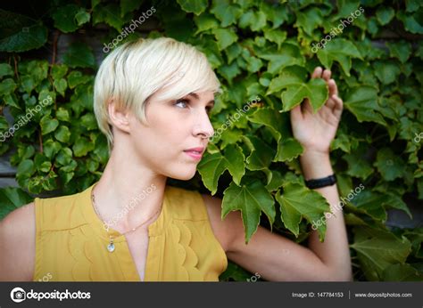 Beautiful Short Haired Platinum Blond Woman Standing Against An Ivy