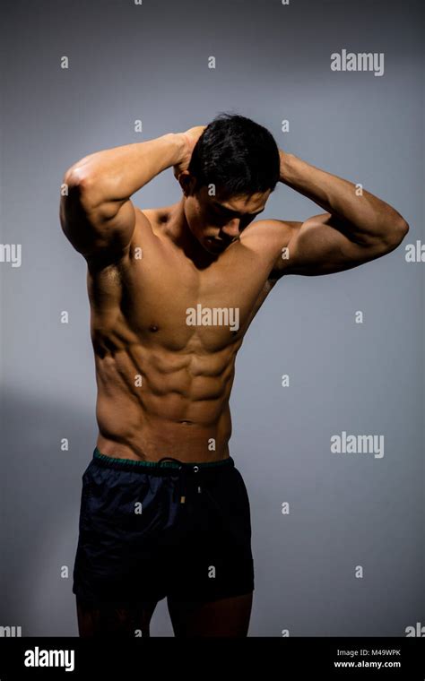 Un modelo asiático muscular fitness flexiona su musculoso abdomen con sus brazos detrás de su