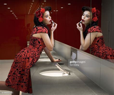 Young Woman Applying Lipstick In Mirror Of Public Lavatory Side View