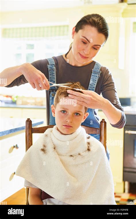 Portrait Unhappy Boy Getting Haircut From Mother In Kitchen Stock Photo