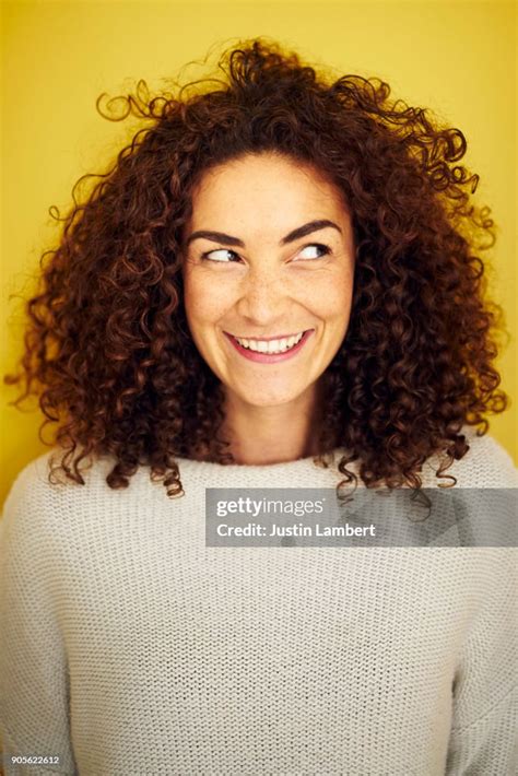 Young Curly Haired Woman Looking Off Camera With A Cheeky Big Smile