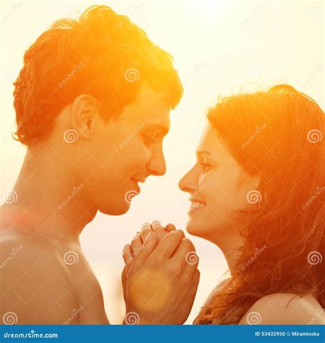 Любящая молодая пара обнимая и целуя на пляже на заходе солнца Стоковое